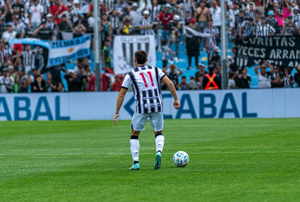 Soccer player number 11 in action on field during a match with cheering fans in the background.
